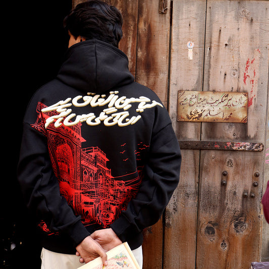 Person wearing a black hoodie with red and white graphics in front of a wooden door.