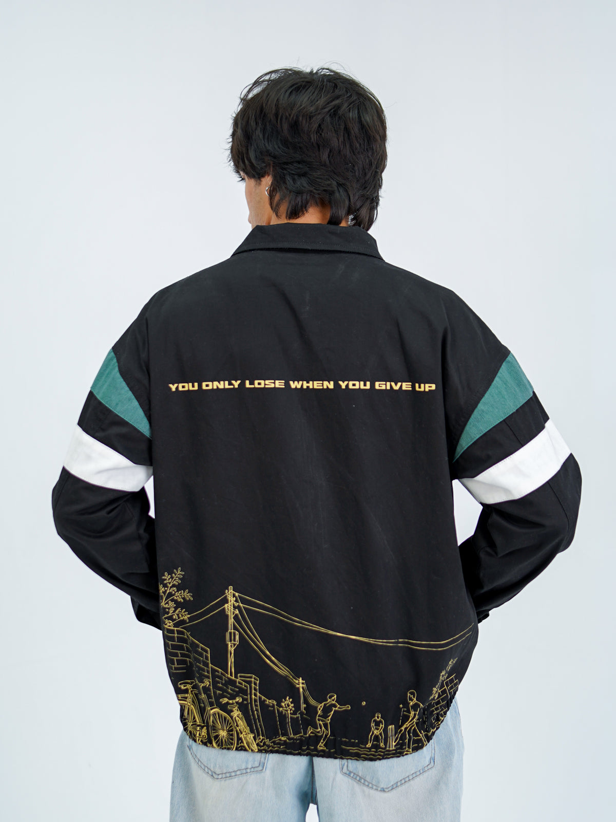 Cornered Tigers '92 jacket hem — gold gali cricket scene with cycles, power lines and brick walls