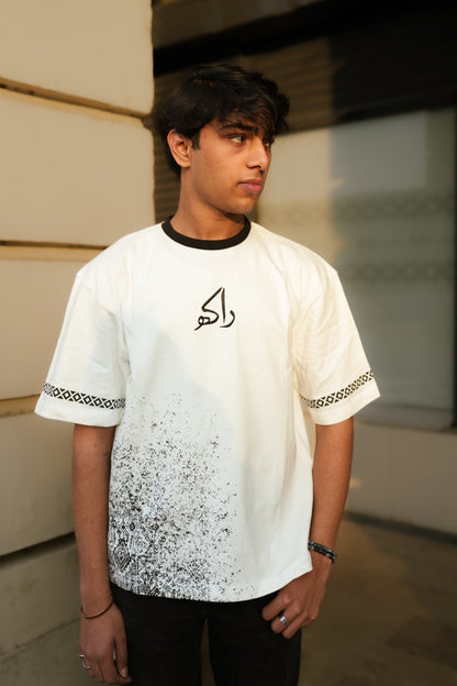 Person wearing a white t-shirt with black text and patterns, standing against a neutral background.